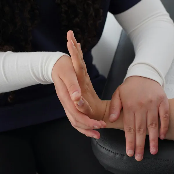 A person assists another with a wrist movement during a physical therapy session